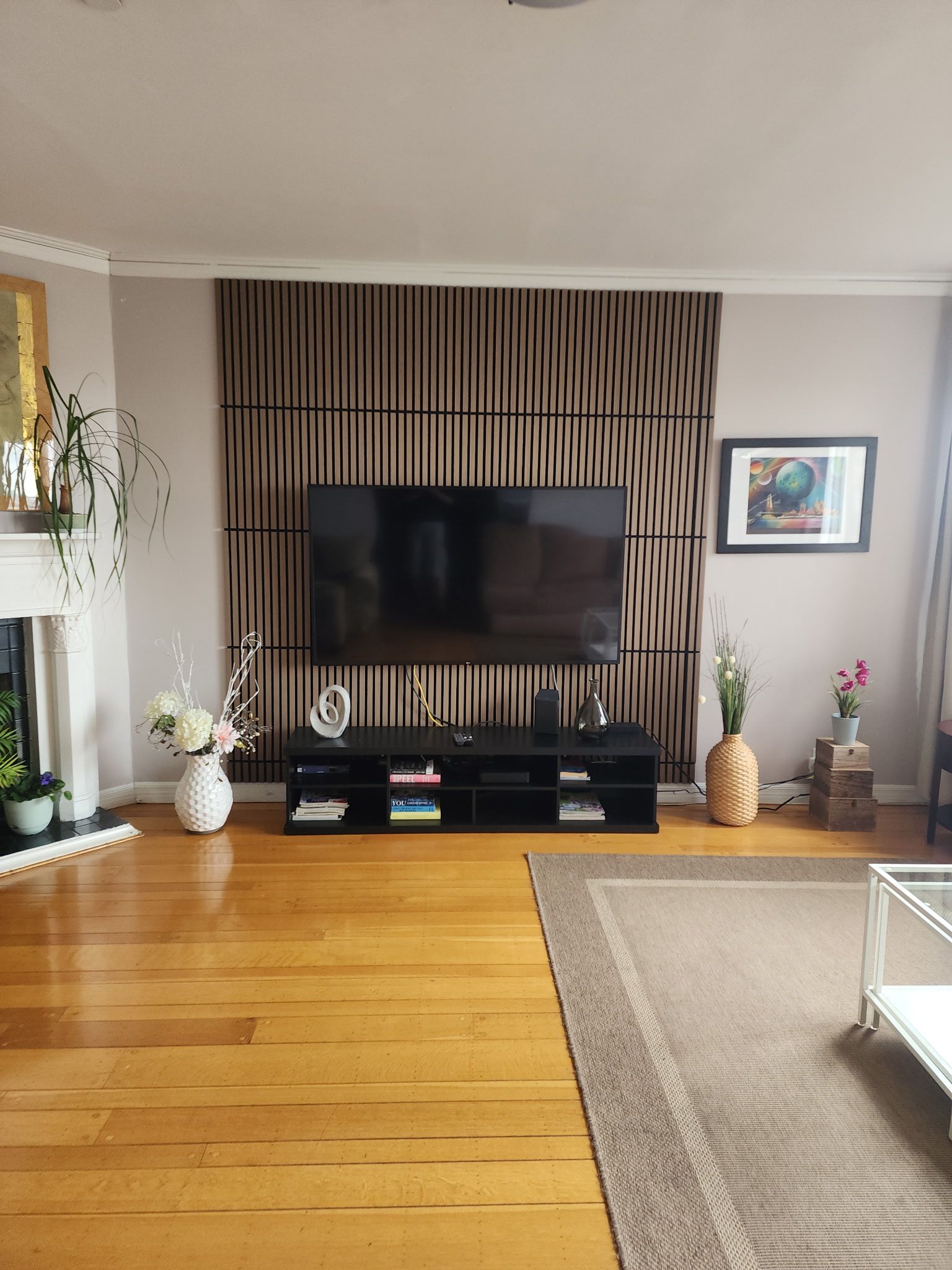 Una sala de estar con un televisor de pantalla plana montado en la pared, un mueble de entretenimiento negro debajo y piso de madera.