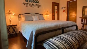 Quarto com cama, luminárias de cabeceira, um adorno na parede e uma porta decorada com um coração.