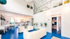A spacious living area with white sofas, a dining table, and a kitchen in the background. - (2027 OPEN!) Beautiful Union Pier Home Steps to Private Beach! (Union Pier)