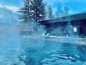 Un bâtiment moderne doté d’une piscine et de chaises longues, entouré d’arbres couverts de neige.