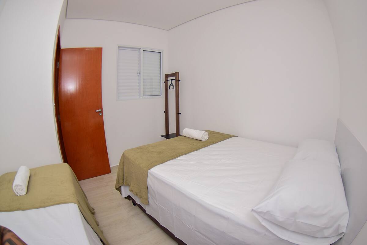 A small, clean room with two beds, a wooden door, and a window with blinds.