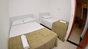 Une chambre d’hôtel avec deux lits, chacun doté d’une tête de lit blanche et d’une couverture marron. Une serviette enroulée est posée sur le lit, au premier plan.