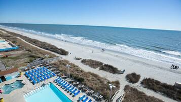 A beach view with a pool area, including lounge chairs and a swimming pool.