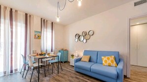 Un salon moderne avec un canapé bleu, un parquet en bois, une table à manger avec des chaises et un miroir décoratif fixé au mur.
