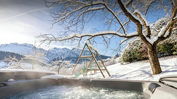 Un bain à remous avec vue sur des montagnes enneigées et, au loin, une balançoire.