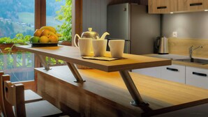 Une cuisine moderne avec un plan de travail en bois, un évier et un réfrigérateur. Une fenêtre offre une vue sur la verdure et les montagnes.
