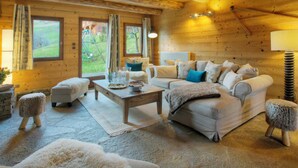 L’intérieur d’un chalet confortable, avec un canapé, un pouf et une table basse, des murs en bois et une vue sur l’extérieur.