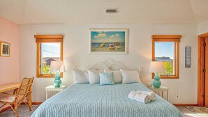 A bedroom with a bed, two bedside tables with lamps, a chair, a painting on the wall, and a window with a view.