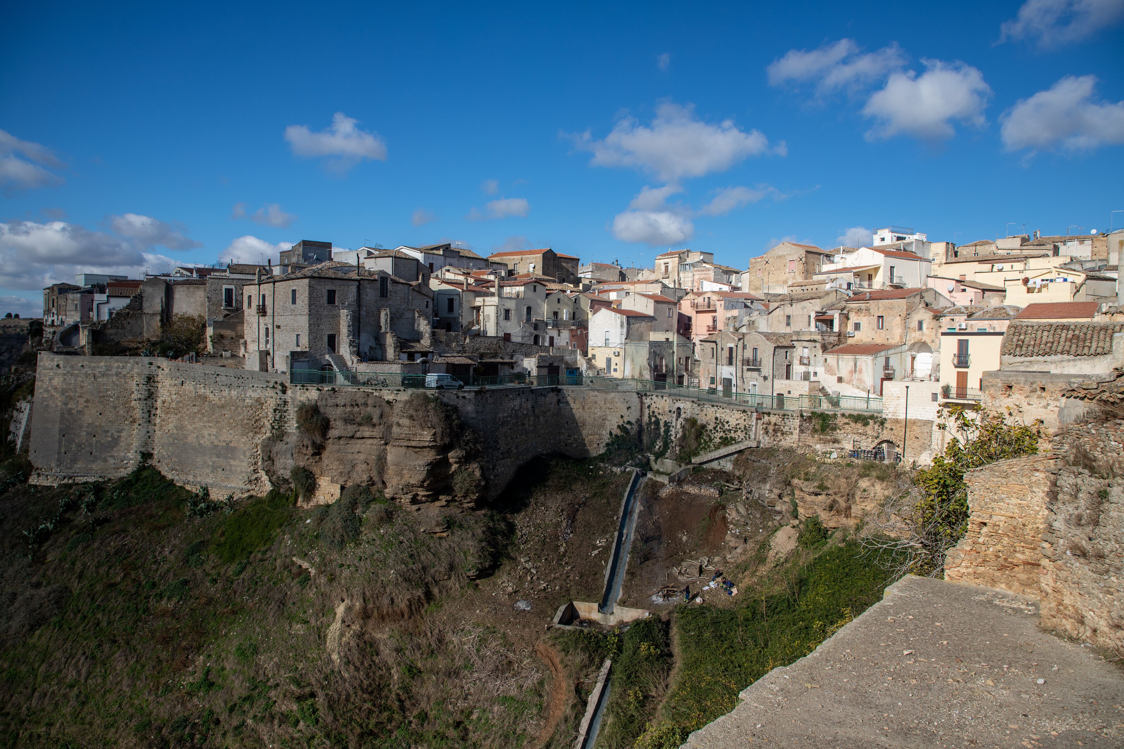 A historic town with ancient stone buildings, a prominent bridge, and a steep cliff.