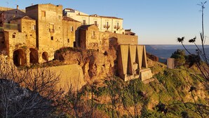 Edificio histórico de piedra con múltiples arcos y una estructura fortificada, con vistas a un paisaje montañoso.