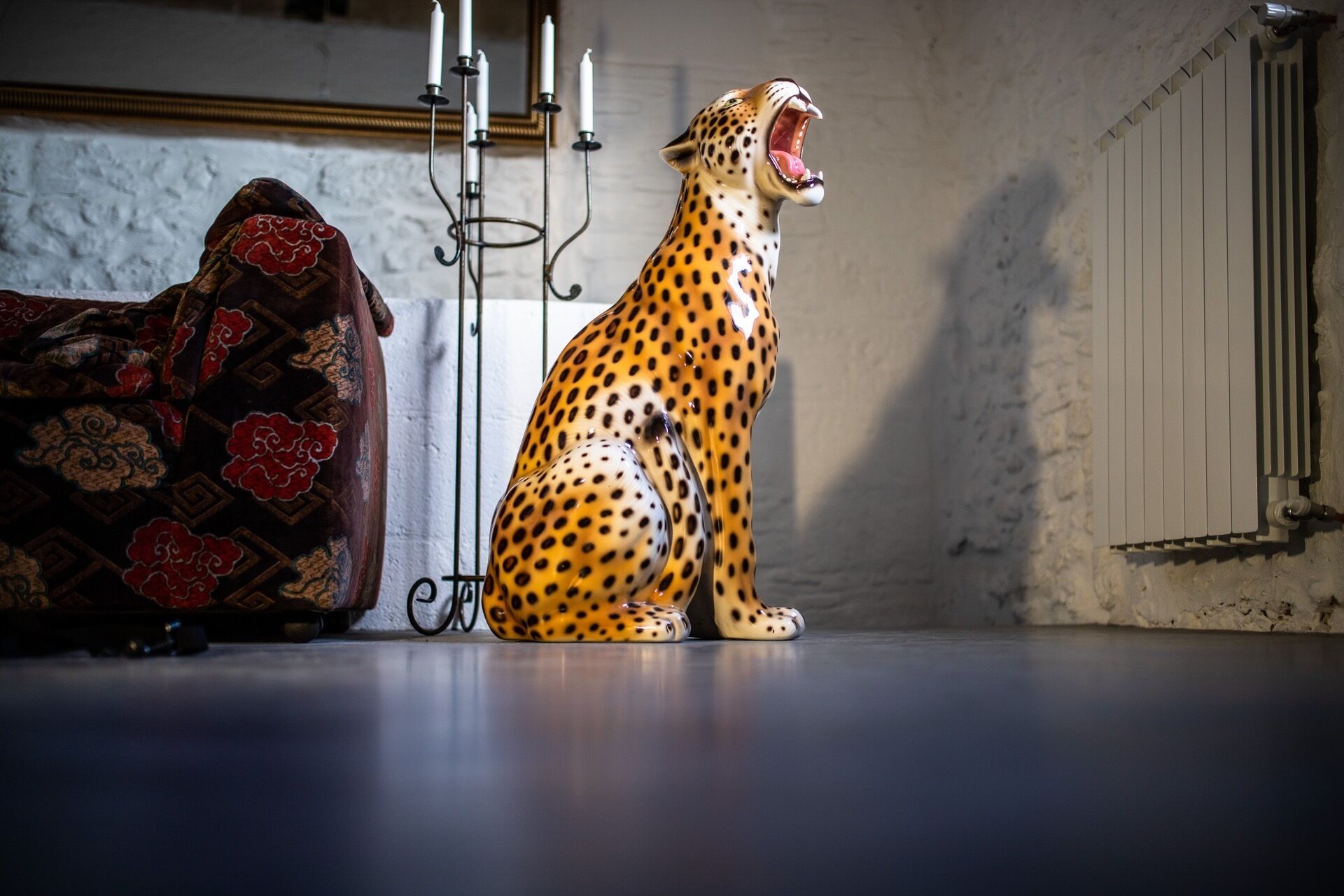 A leopard statue in a room with a patterned sofa and a radiator.