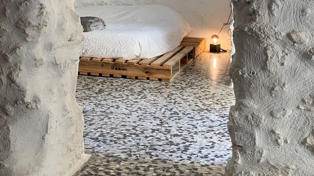 Un dormitorio con pared de piedra rústica, estructura de cama de madera y suelo de baldosas de mosaico.