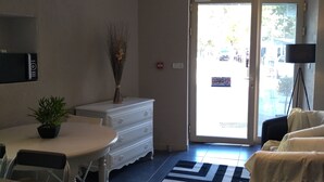 A hotel lobby with a reception desk, a white sofa, a small table with a plant, a television on a tripod, and a large window with a view of the street. - Hôtel Renaissance Martigues (Martigues)