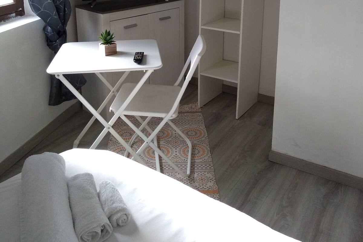 A small, neatly arranged room with a bed, a desk with a chair, a television, and a wardrobe.