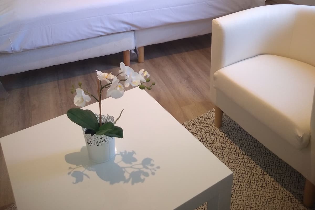 A hotel room with a large bed, a bedside table with a lamp, a white armchair, and a small table with a potted orchid.