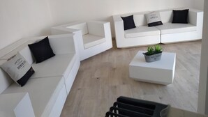 A modern living room with white sofas and black cushions, a small coffee table with a plant, and a staircase leading to another level. - Hôtel Renaissance Martigues (Martigues)