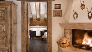 Ein rustikales Badezimmer mit Badewanne, Holzschränken und einem Kamin mit Feuer.