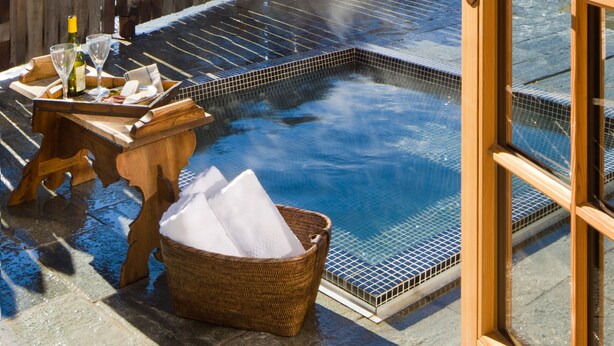 Wellnessbereich mit Whirlpool, Holzterrasse und Blick auf schneebedeckte Berge.