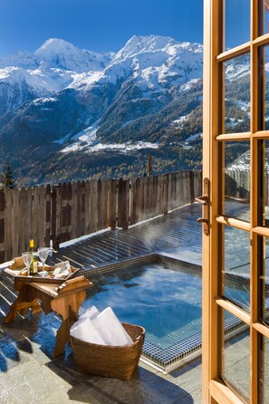 Zona de spa con hidromasaje, terraza de madera y vistas a montañas nevadas.