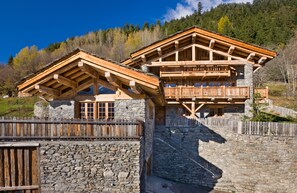 Una cabaña de madera con paredes de piedra, un balcón y una escalera de piedra que conduce a la entrada.