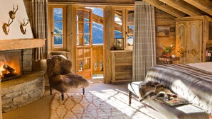 Ein gemütliches Zimmer mit Kamin, einem Fellstuhl, einem Bett und Bergblick.