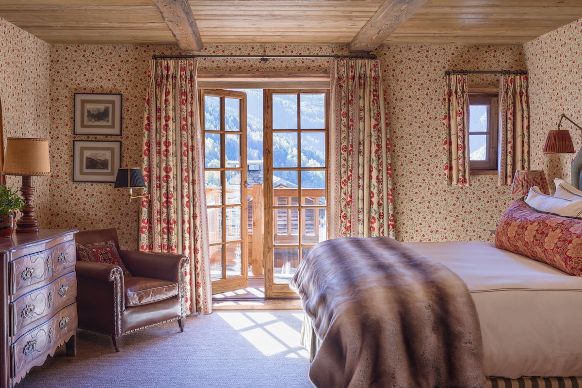 Una habitación con cama, cómoda de madera, una silla y ventana con vista a montañas.