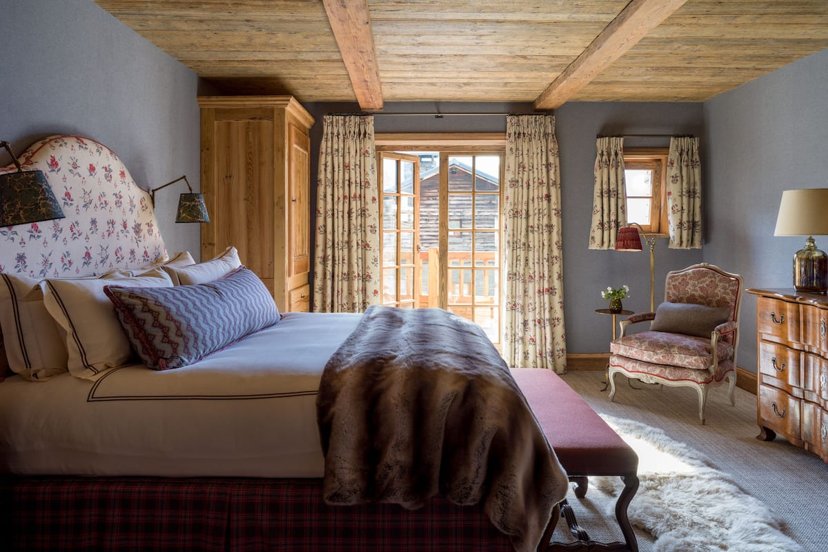 Un dormitorio con cama, una silla, cómoda y ventana con cortinas.
