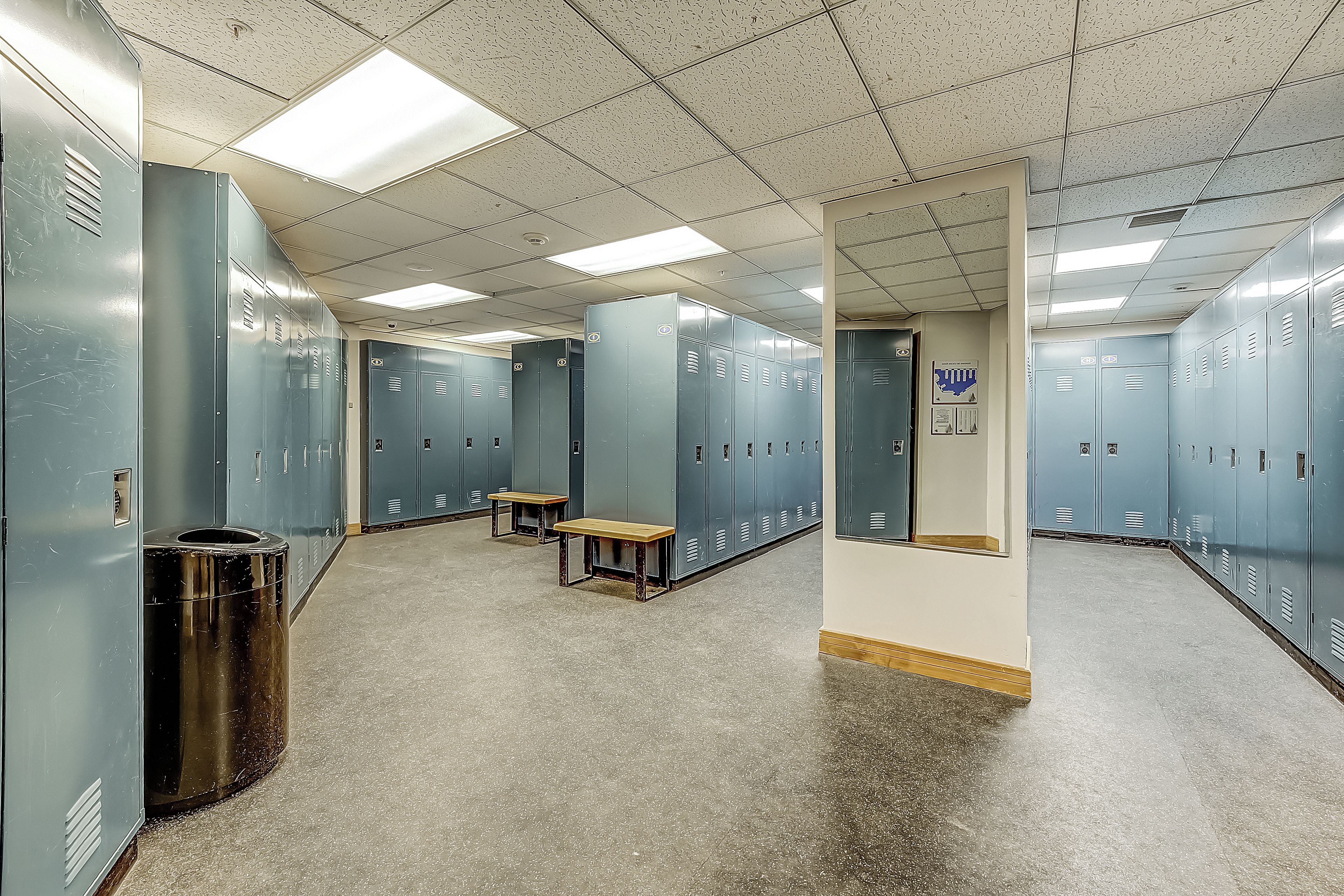 Un vestiaire équipé de plusieurs casiers, d’une poubelle et de deux bancs.