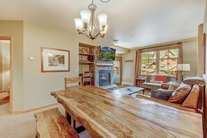 Un vaste espace de vie comprenant une grande table à manger en bois, une cheminée et une vue sur un paysage montagneux par les fenêtres.
