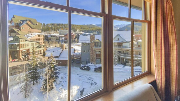 Une vue depuis une fenêtre donnant sur une ville enneigée, avec des bâtiments et une montagne en arrière-plan.