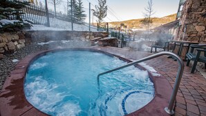 Un bain à remous entouré d’un muret en pierre et d’une terrasse en bois.