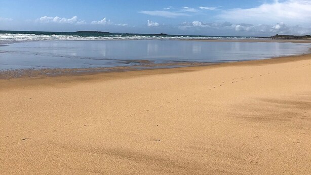 Ampia spiaggia sabbiosa con onde delicate e cielo azzurro intenso.