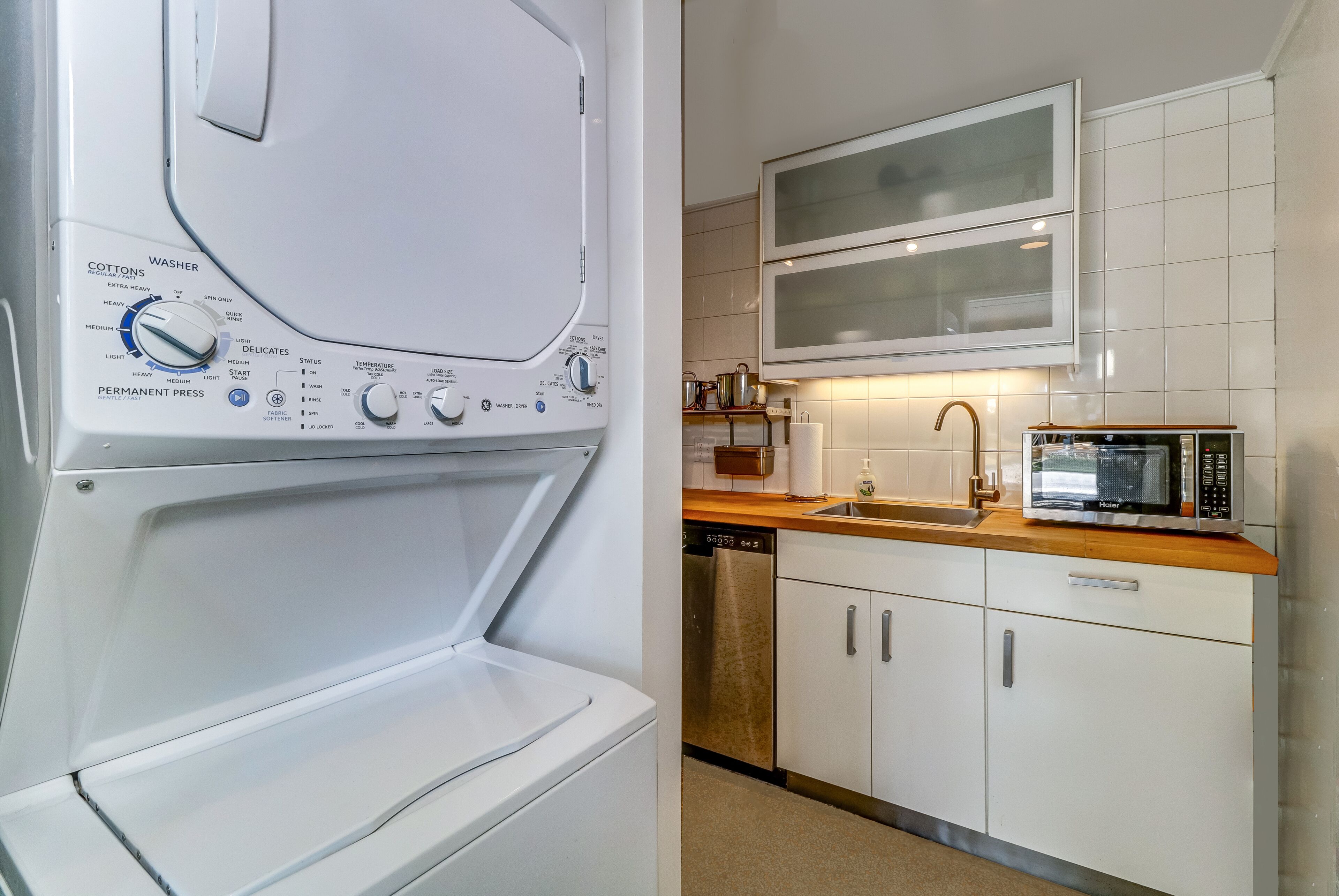 Une cuisine moderne équipée d’un lave-linge et d’un sèche-linge intégrés, d’un four à micro-ondes et d’un évier en acier inoxydable.
