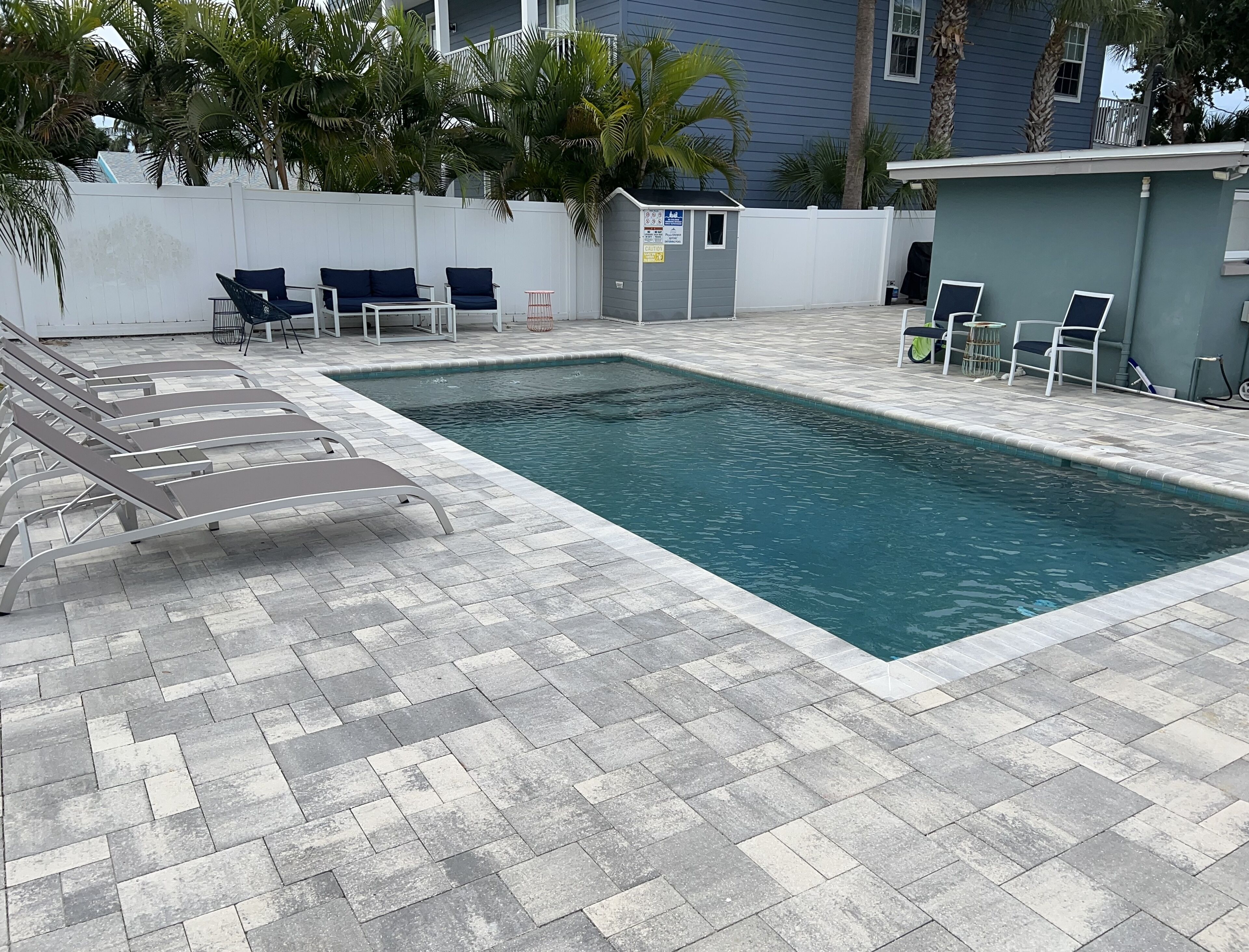 A rectangular swimming pool with a tiled deck, surrounded by lounge chairs and a small structure with a sign.