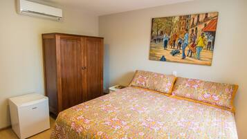 A bedroom with a bed, an air conditioner, a wardrobe, and a painting on the wall.