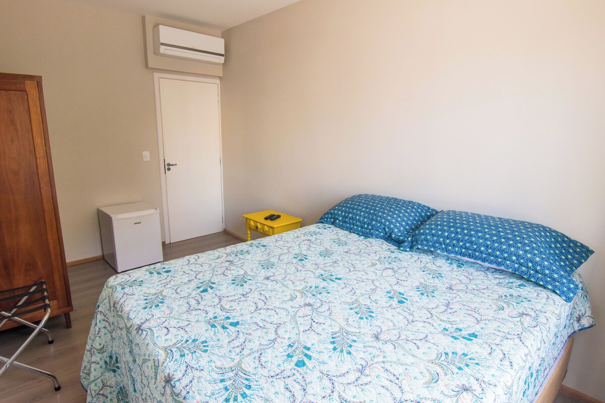 A bedroom with a bed, a small bedside table, a wardrobe, and an air conditioning unit.