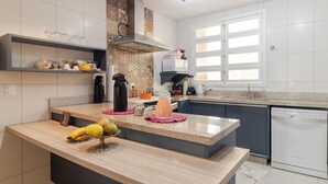 Une cuisine moderne dotée d’un îlot central, d’appareils électroménagers intégrés et d’une fenêtre avec stores.