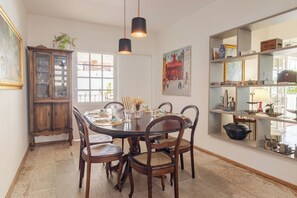 A dining area with a round table, chairs, a cabinet, and a shelf with various items. - Hospedaria Conceitual (Florianópolis)