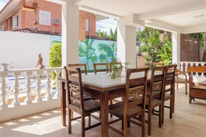 An outdoor dining area with a white table and wooden chairs, surrounded by a white railing, with a view of a mural and greenery. - Hospedaria Conceitual (Florianópolis)