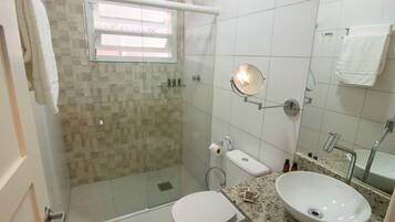Un baño con ducha de vidrio, inodoro, lavamanos con espejo y un perchero para toallas.