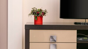 Un centre d'entreteniment modern amb un televisor de pantalla plana, un vas vermell amb flors i un armari negre i beix amb calaixos.