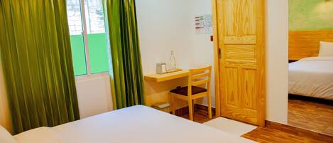 A hotel room with a bed, a desk with a chair, a wooden wardrobe, and a window with curtains.