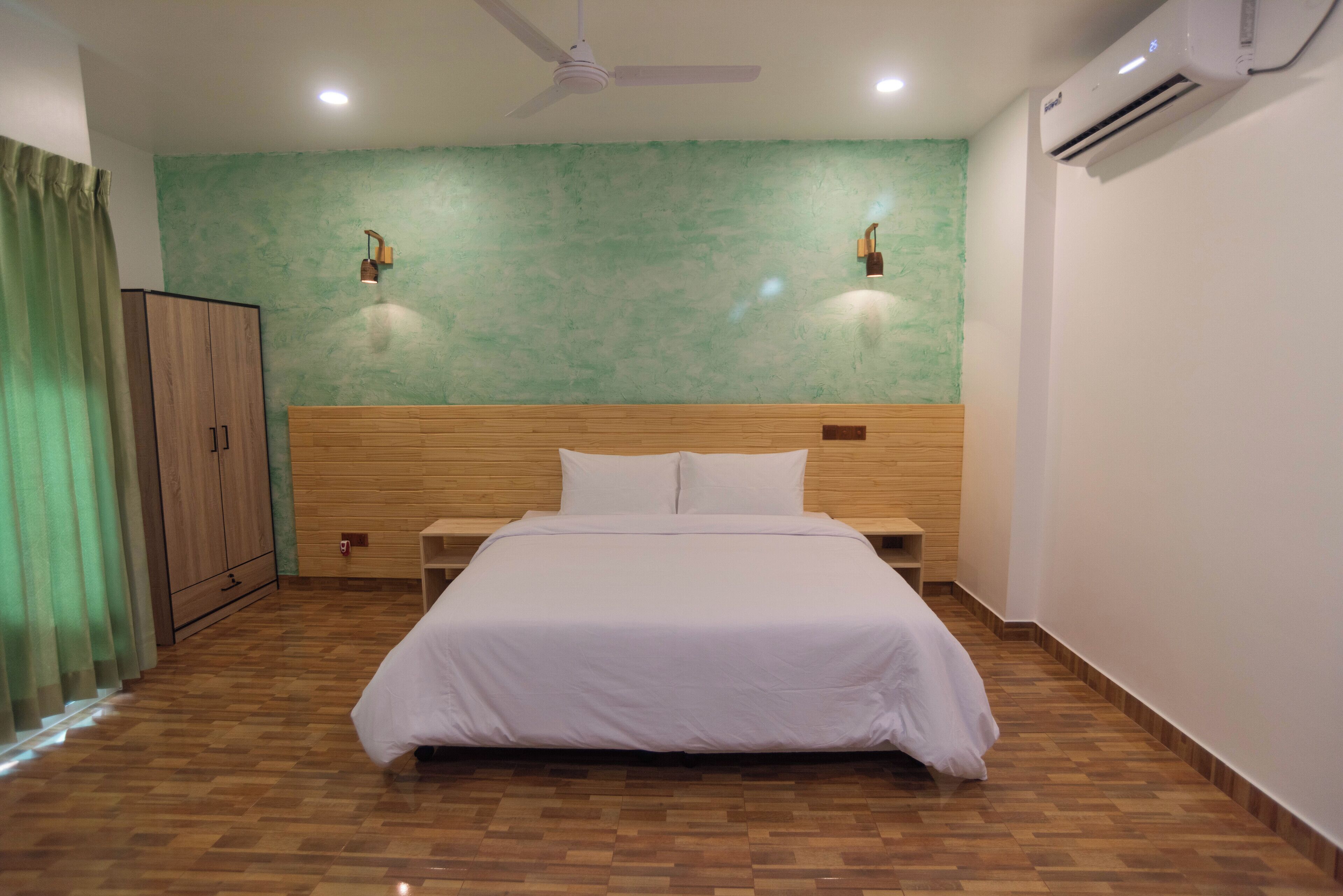 Une chambre avec une tête de lit en bois, un lit avec une literie blanche, deux lampes fixées au mur, un climatiseur et un ventilateur de plafond.