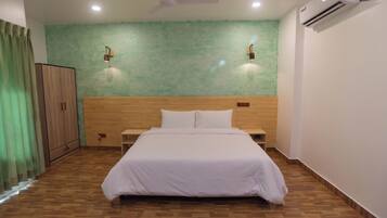 Une chambre avec une tête de lit en bois, un lit avec une literie blanche, deux lampes fixées au mur, un climatiseur et un ventilateur de plafond.