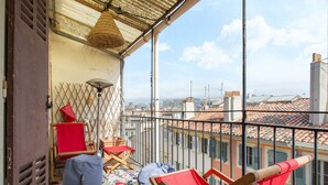 Un balcon avec des chaises rouges, un pouf bleu et un tapis à motifs.