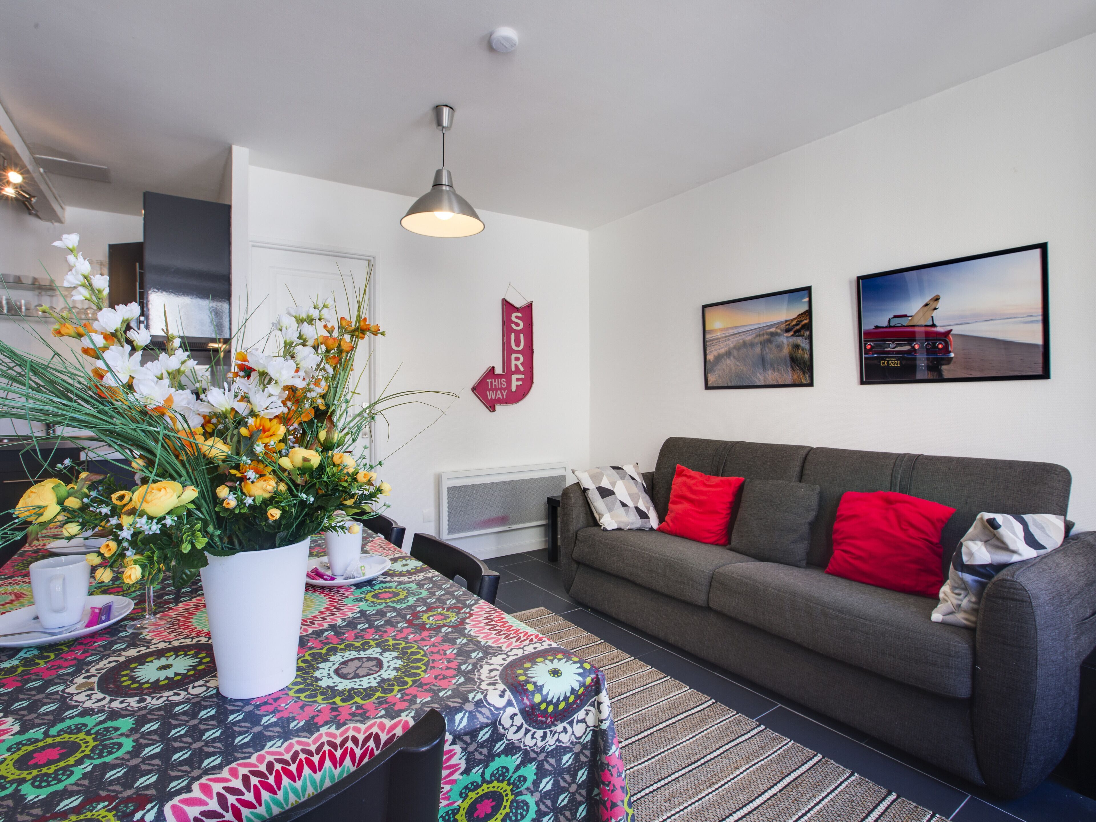 A modern living room with a grey sofa, colorful tablecloth, and a decorative flower arrangement.