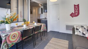 A dining area with a table set for four, a kitchen in the background, and a 'SURF THIS WAY' sign on the wall.
