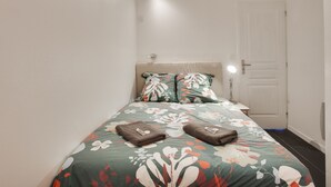 A small, neatly arranged bedroom with a bed, pillows, and a bedside table with a lamp.