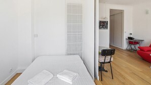 Une petite pièce propre, avec un lit, une chaise et un canapé rouge.