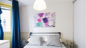 Ein Schlafzimmer mit Bett, Nachttisch, Lampe und einem Fenster mit Vorhängen.
